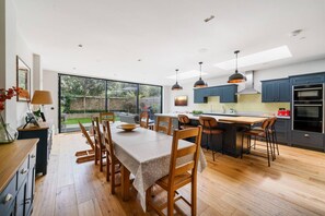 A modern kitchen with a dining area, featuring a large island, pendant lighting, and a view of the outdoors.