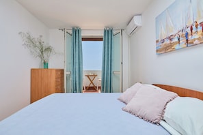 A bedroom with a bed, a wooden dresser, a potted plant, a painting, and a balcony with a table and chairs. - Vista Del Mare - Two Bedroom Apartment, Sleeps 4 (Dubrovnik)