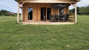 Una cabaña de madera con un porche techado, una mesa con sillas y un gran paraguas.