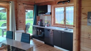 Interior de una cabaña de madera con cocina, comedor y vistas al exterior.