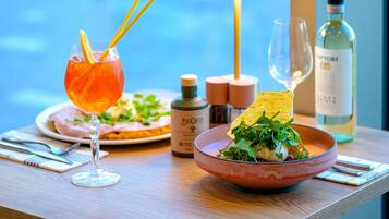 Una mesa con una copa de cóctel, una botella de vino, una lámpara y un bol de ensalada.
