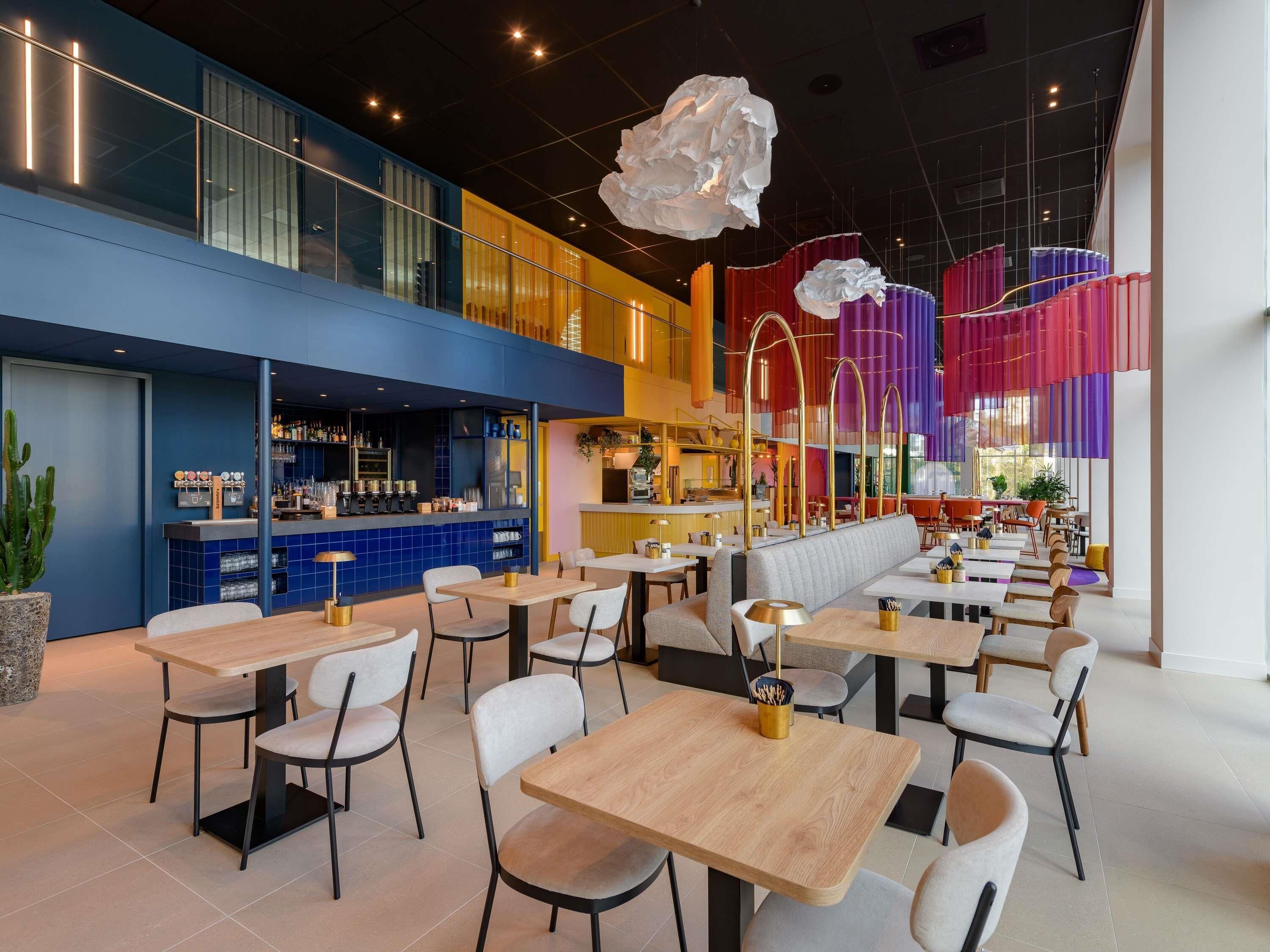 Um restaurante moderno com várias áreas de refeições, um bar e disposição de mesas e cadeiras.