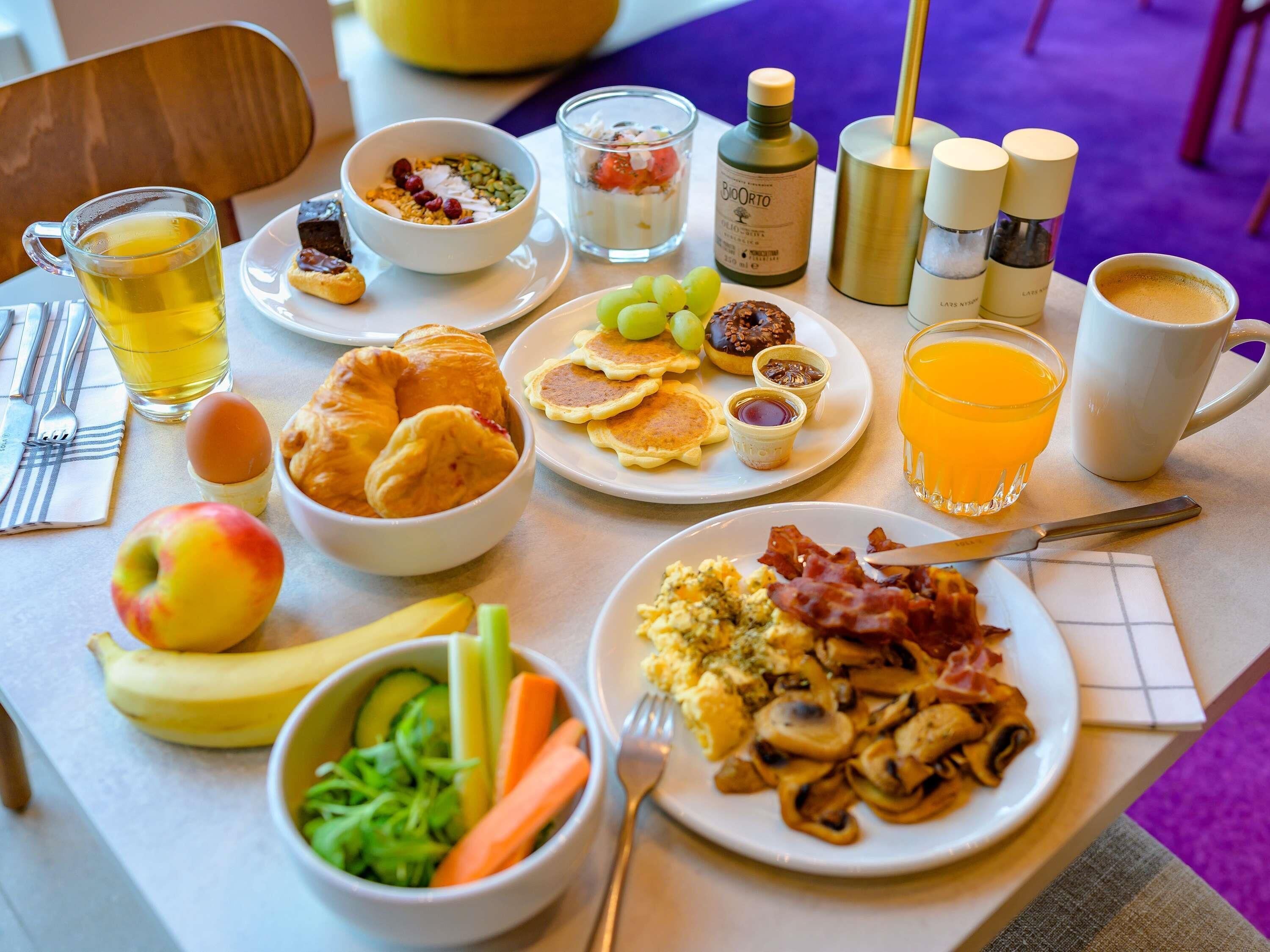 Un ricco buffet per la colazione con diverse pietanze, tra cui uova, pancetta, pancakes e frutta fresca.