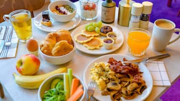 Un ricco buffet per la colazione con diverse pietanze, tra cui uova, pancetta, pancakes e frutta fresca.