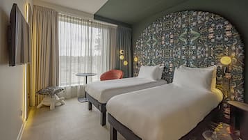 A hotel room with two beds, a TV, a small table, a chair, and a large decorative wall.