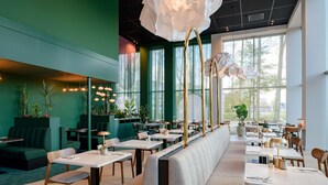 A modern restaurant with green walls, large windows, and a central seating area with tables and benches. - Ibis Styles Rotterdam Ahoy (Rotterdam)