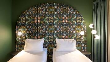 Una habitación con dos camas, un cabecero estampado y un espejo con iluminación.