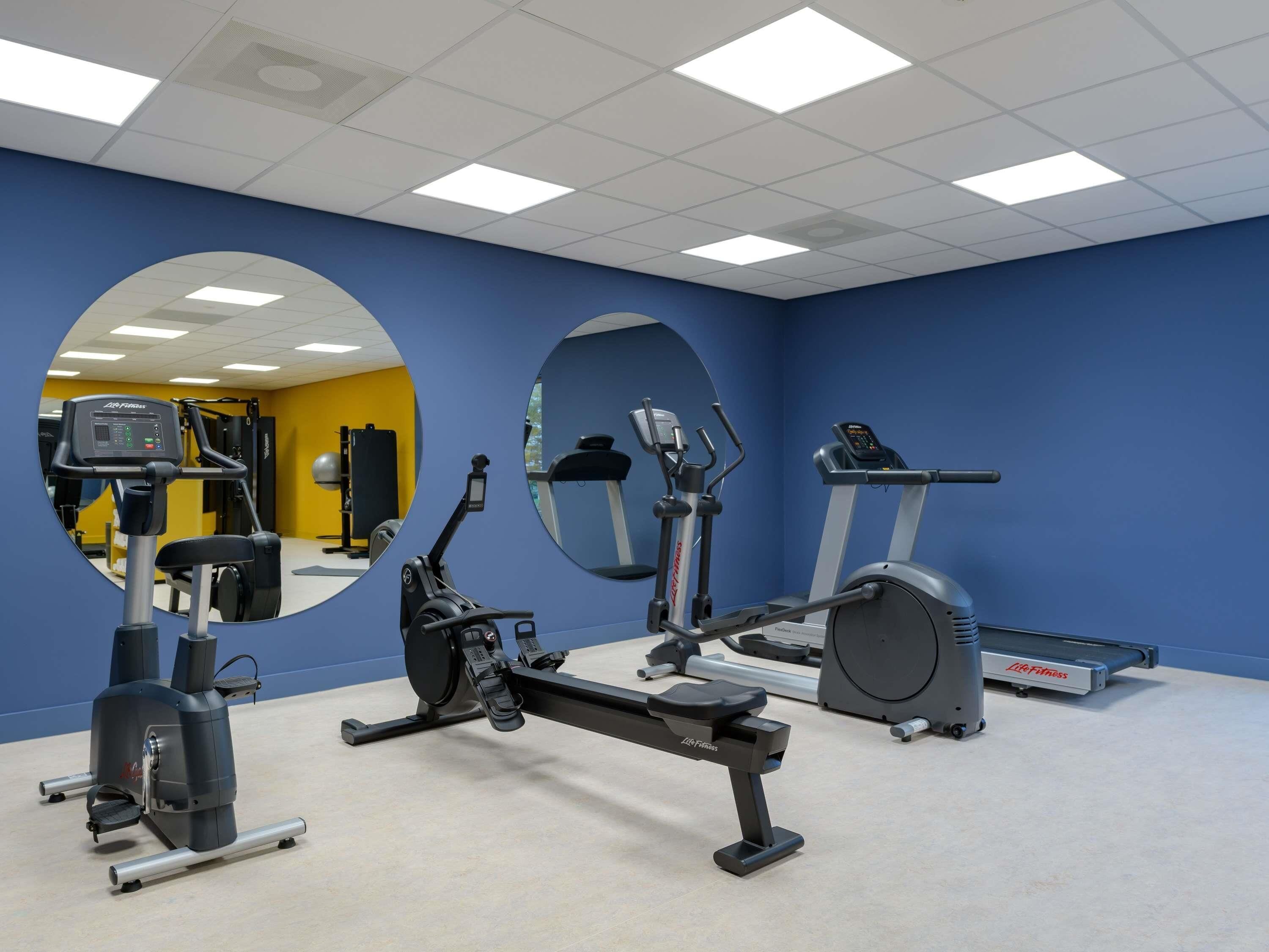 Un gimnasio con equipo de ejercicio, espejos y una pared amarilla.