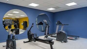 Un gimnasio con equipo de ejercicio, espejos y una pared amarilla.