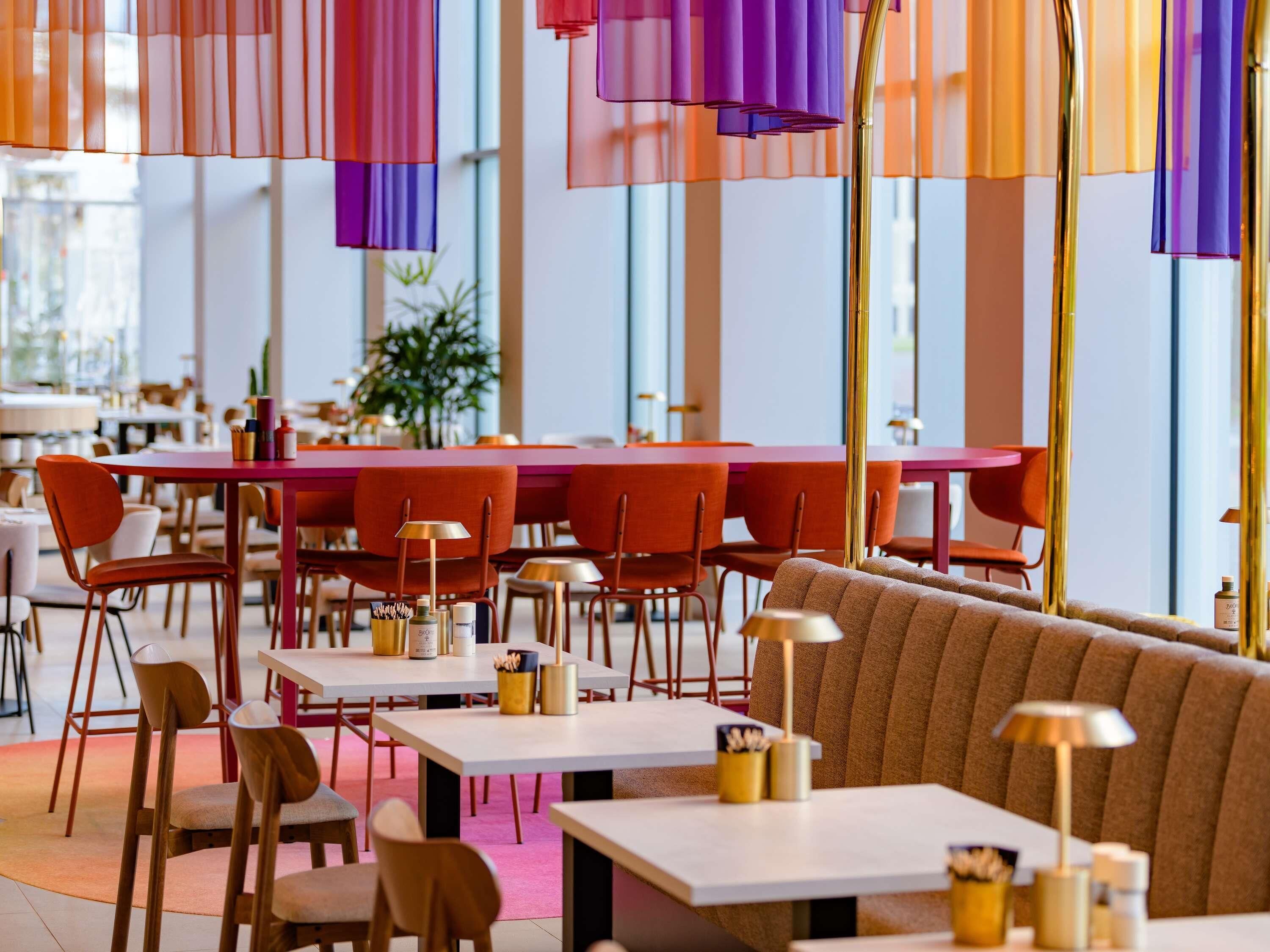 A modern restaurant interior with high tables and chairs, a central seating area, and pendant lighting.