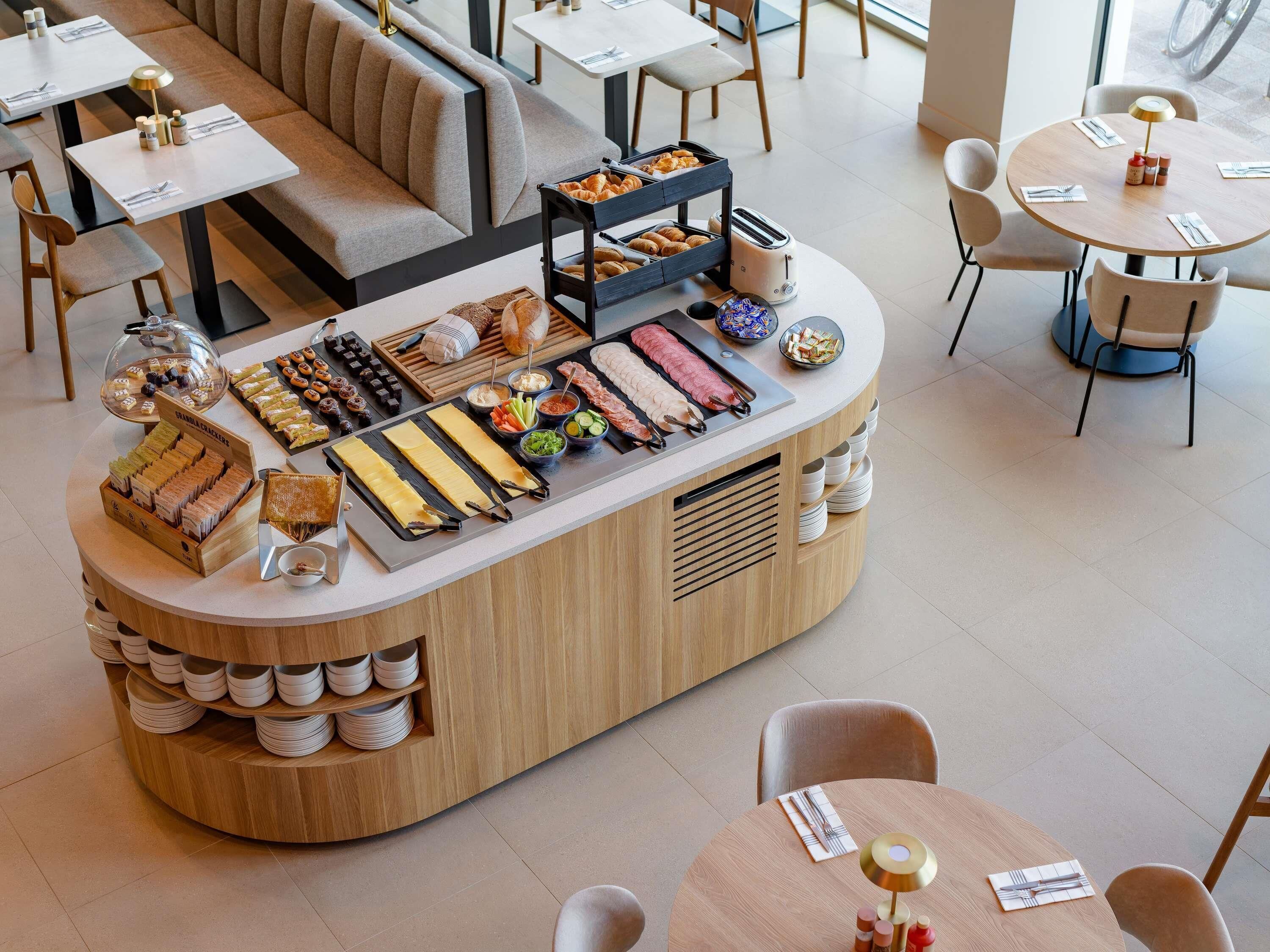 A breakfast buffet with various food items, a seating area with tables and chairs, and a counter with a display of bread and pastries.