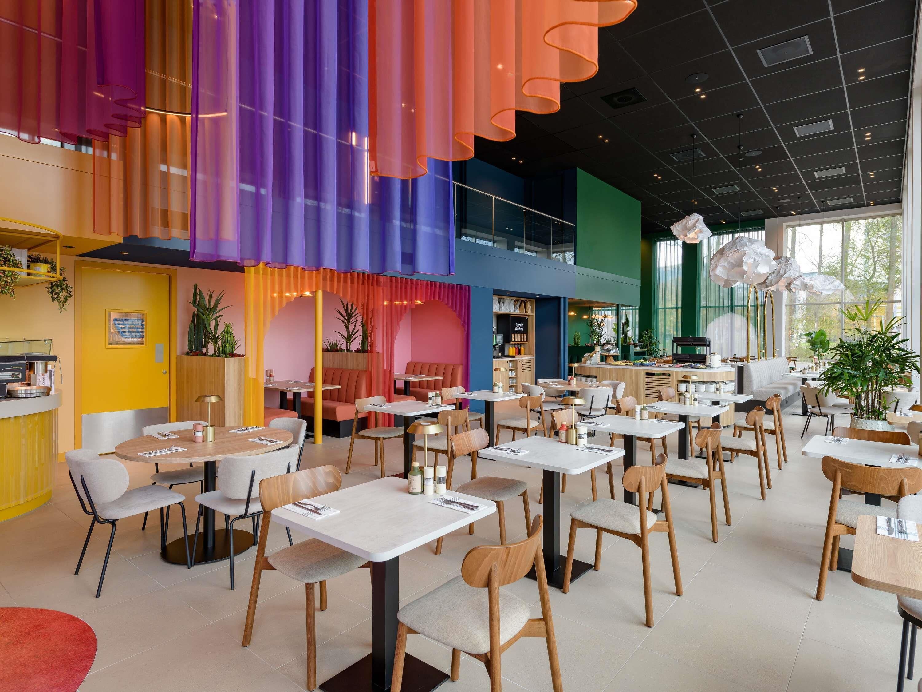 A modern restaurant with multiple dining areas, including booths and tables, and a bar area.