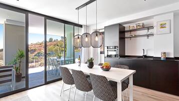 A modern kitchen with a dining area, large windows, and a view of the outdoors.