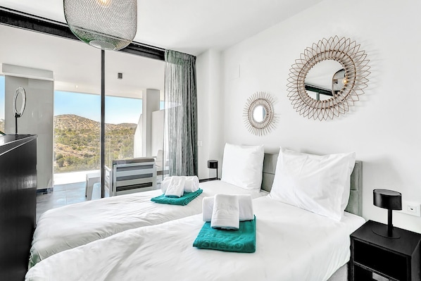 Een moderne hotelkamer met twee bedden, een groot raam met uitzicht op een heuvellandschap en decoratieve wandkunst.