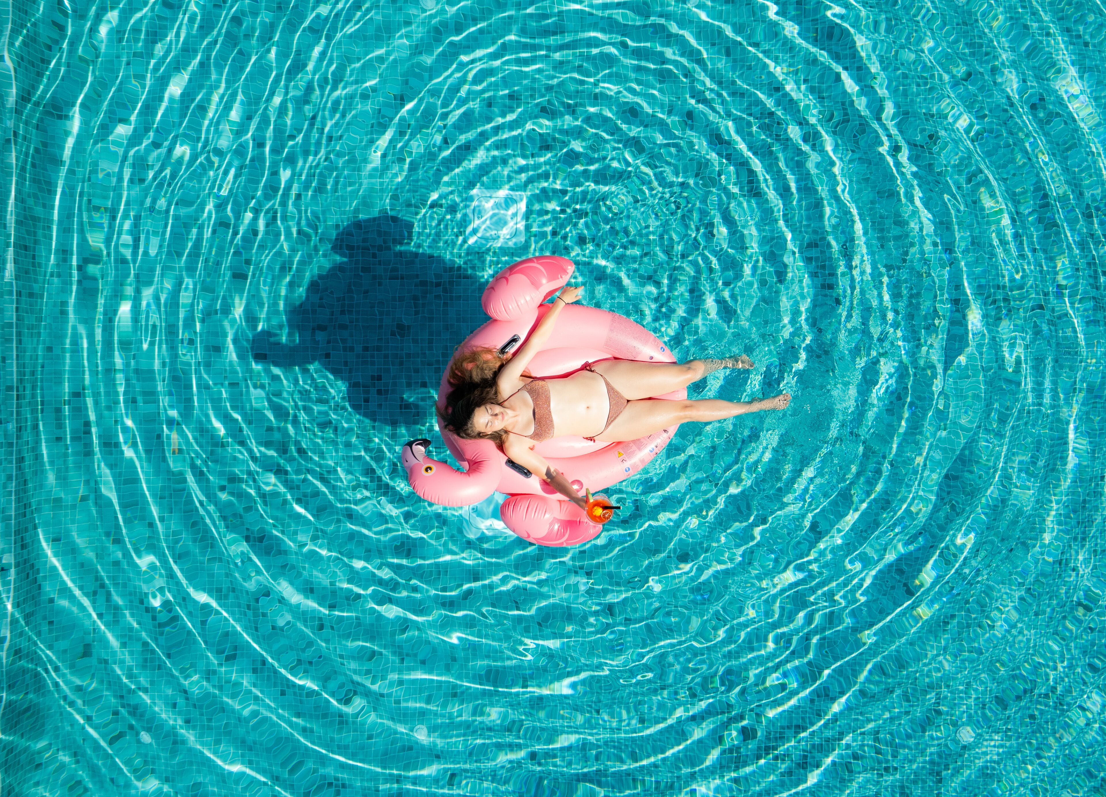 A person floating in a pool with a pink flamingo float.
