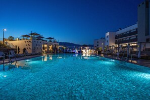 A swimming pool with tiled flooring, surrounded by lounge chairs and umbrellas, with buildings in the background. - Hacienda el Sueño - Holiday Resort (Mijas)