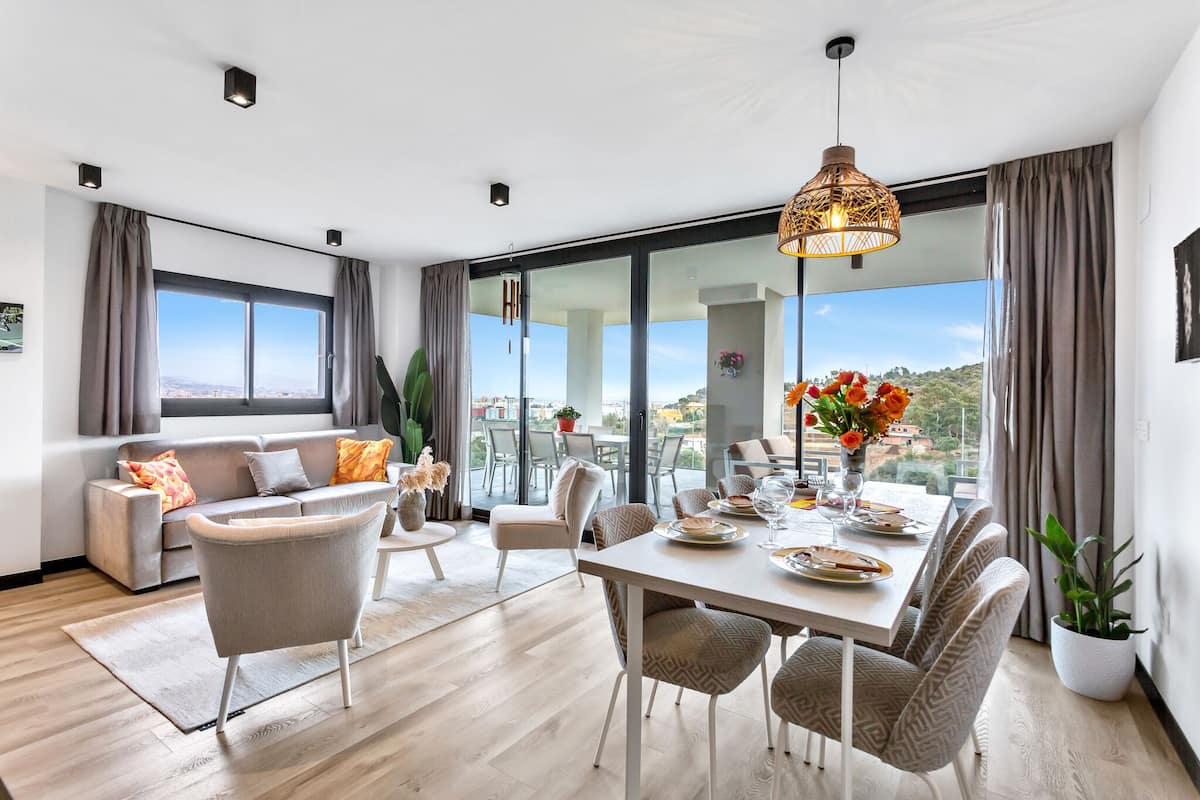 A modern living room with a dining area, large windows, and a view of the city.
