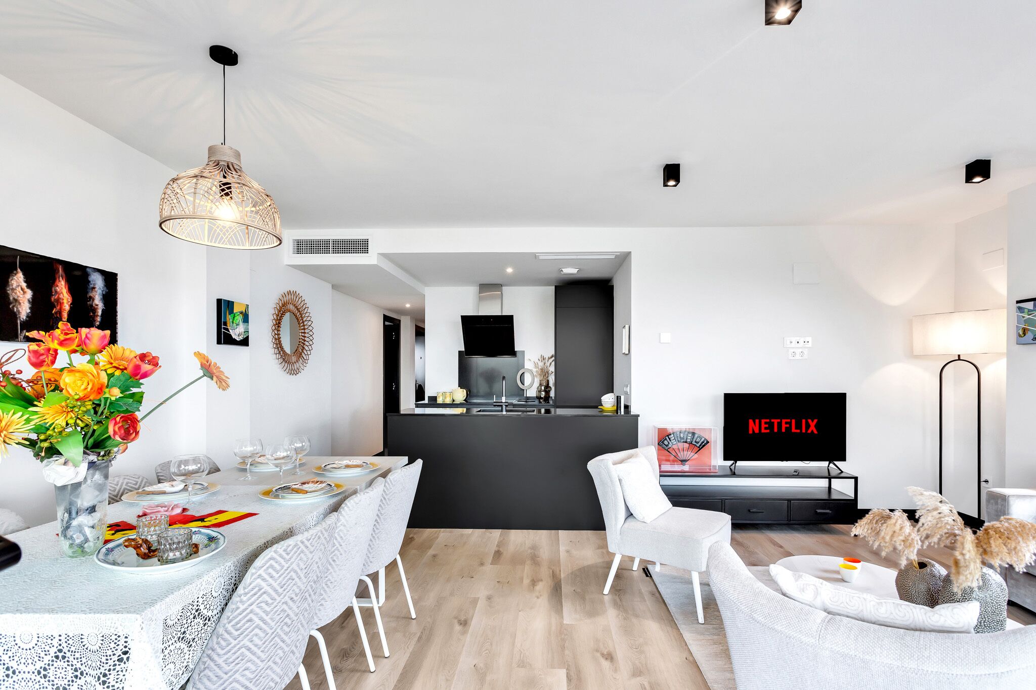 Een moderne woonkamer met een eetgedeelte, een keuken en een tv waarop 'NETFLIX' wordt weergegeven.