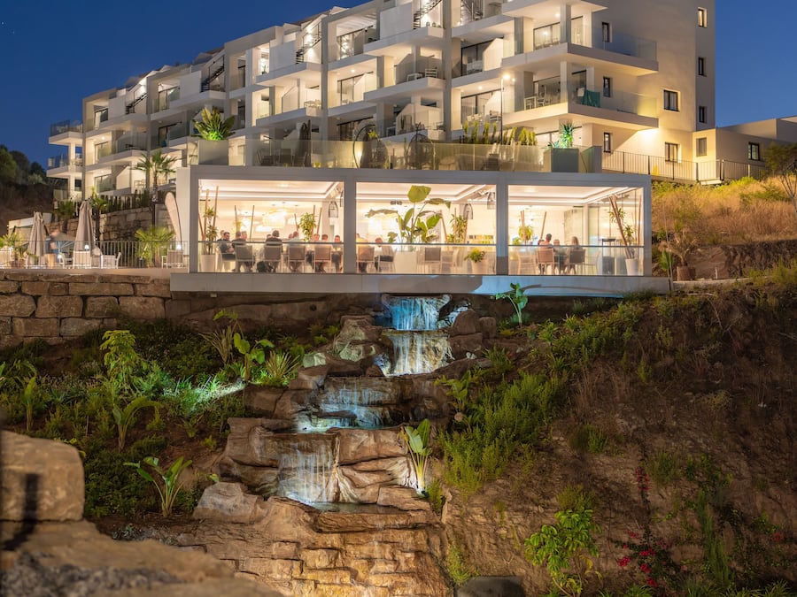Een hotel met meerdere verdiepingen, balkons, een eetgedeelte en een waterval.
