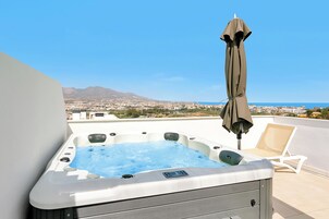 A hot tub with a city view, an umbrella, and a lounge chair on a rooftop.