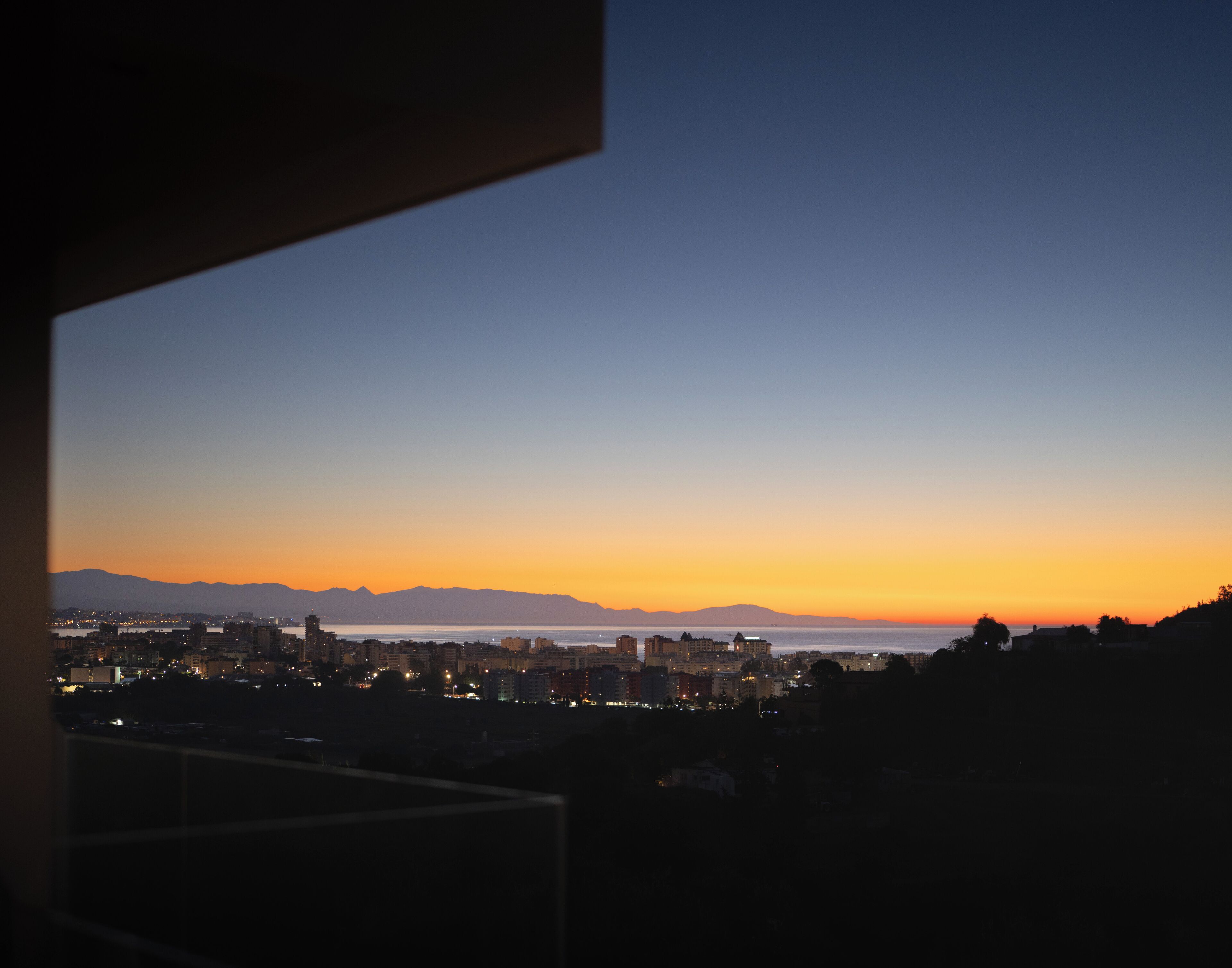 A cityscape at dusk with a view of the water and mountains in the distance.