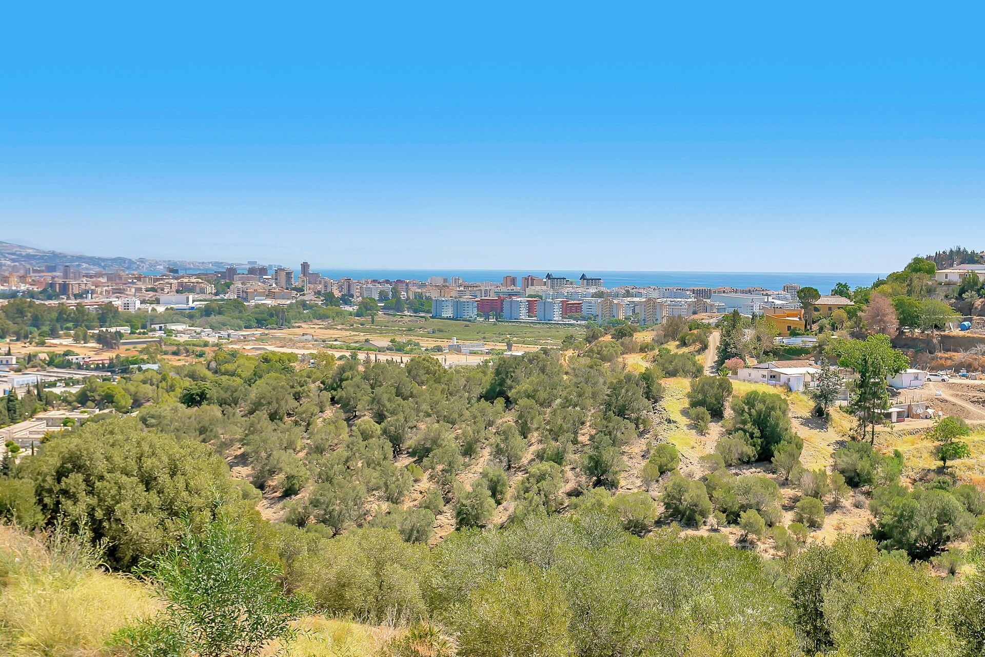 A coastal cityscape with dense urban buildings, a clear blue sky, and a mix of urban and natural landscapes.