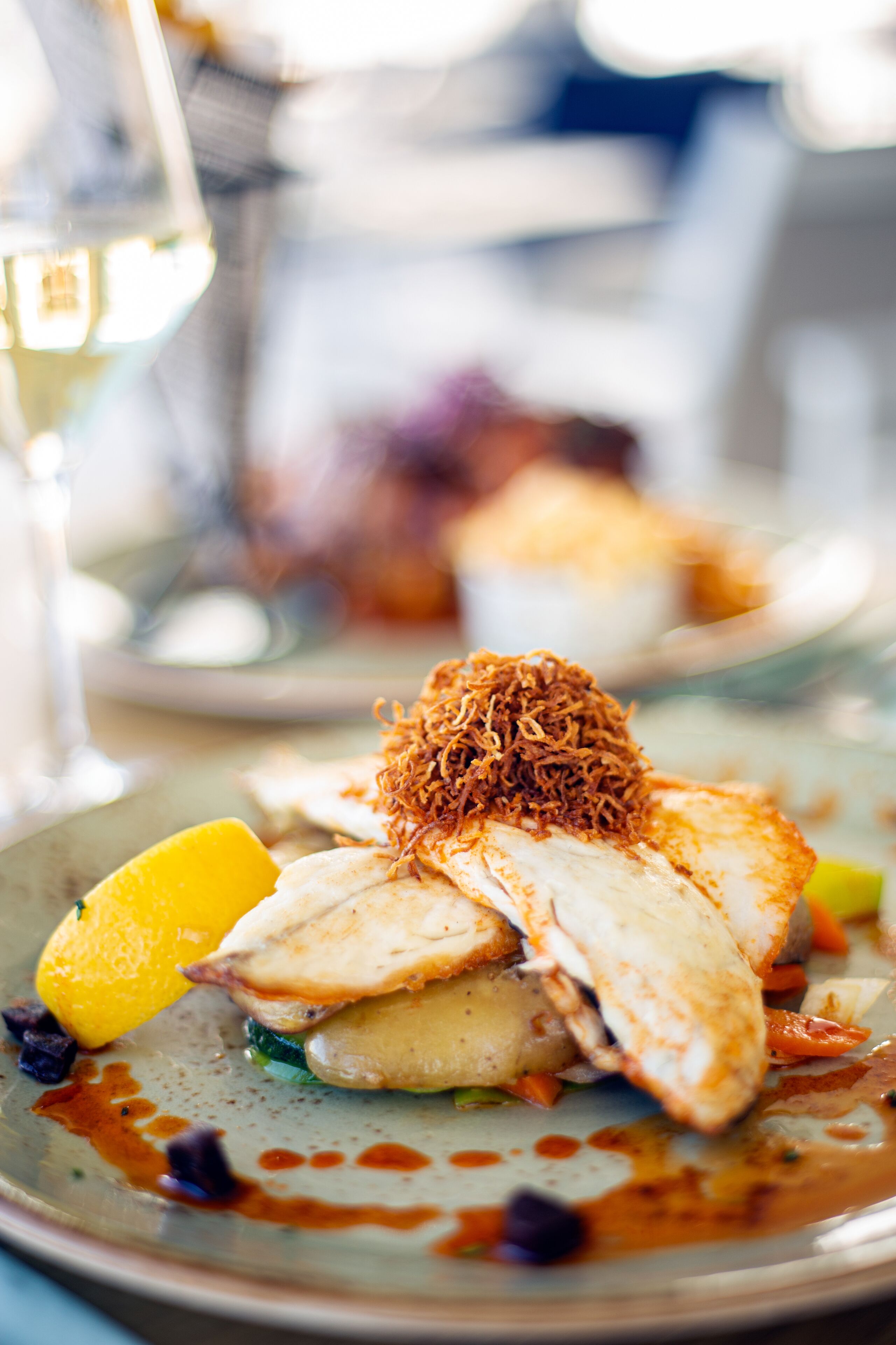 Un plato de comida con un gajo de limón, un trozo de pescado y cebollas fritas como guarnición.