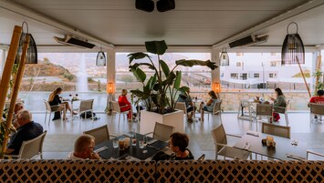 A restaurant with outdoor seating, large windows, and a central plant.