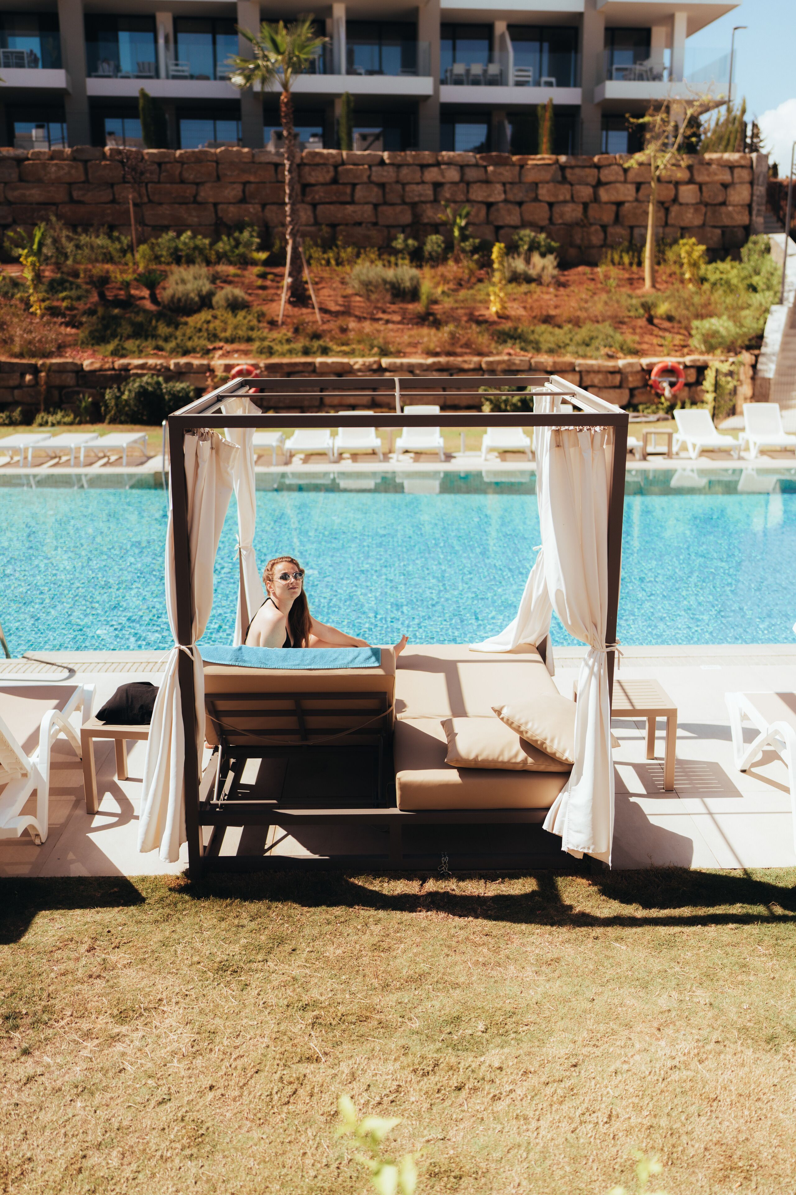 A poolside area with a canopy, lounge chairs, and a view of a building in the background.