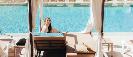 A poolside area with a canopy, lounge chairs, and a view of a building in the background.