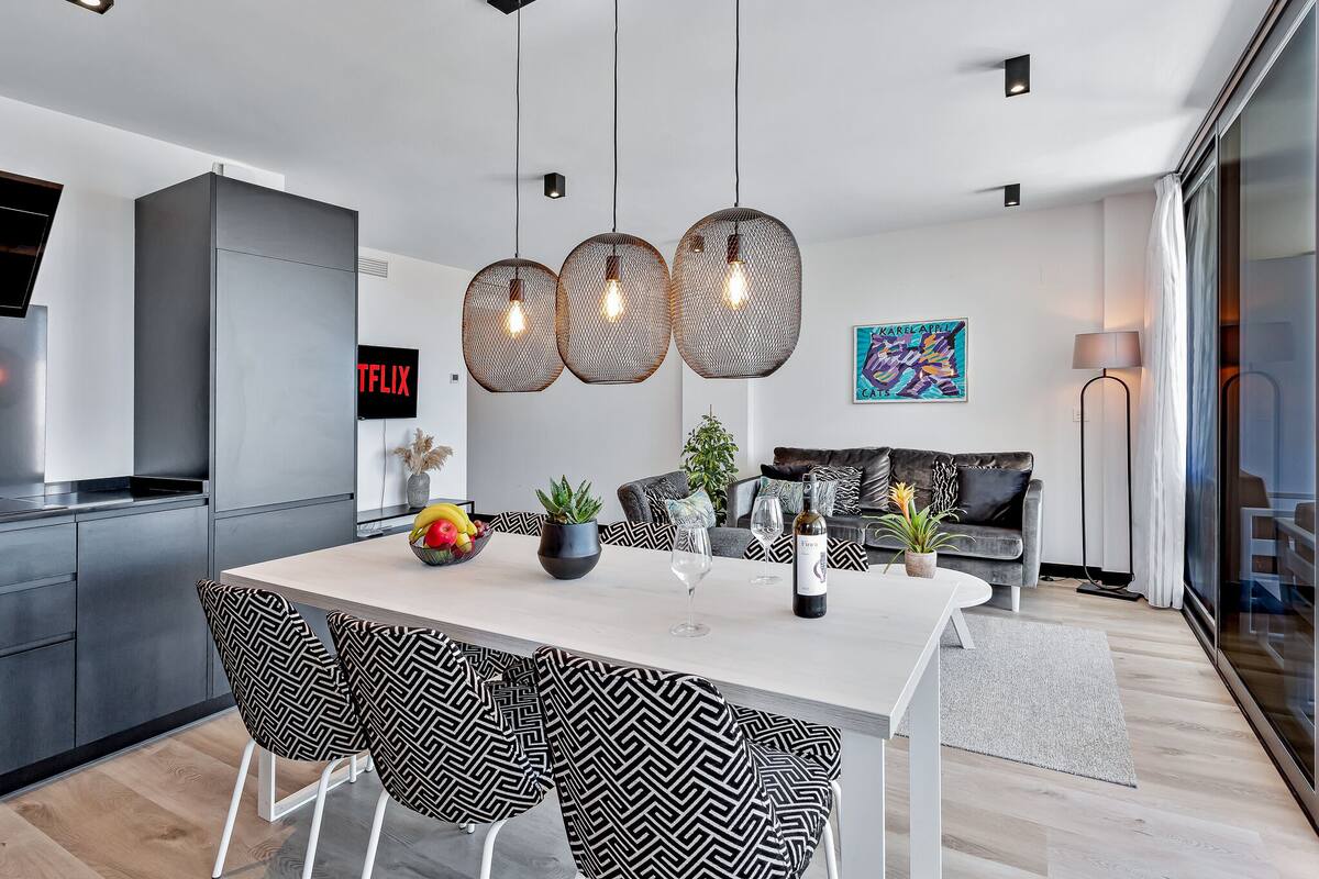 A modern kitchen with a white countertop, black and white patterned chairs, and hanging wicker pendant lights.