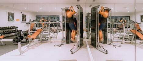 A gym with mirrored walls, exercise equipment, and weight racks.