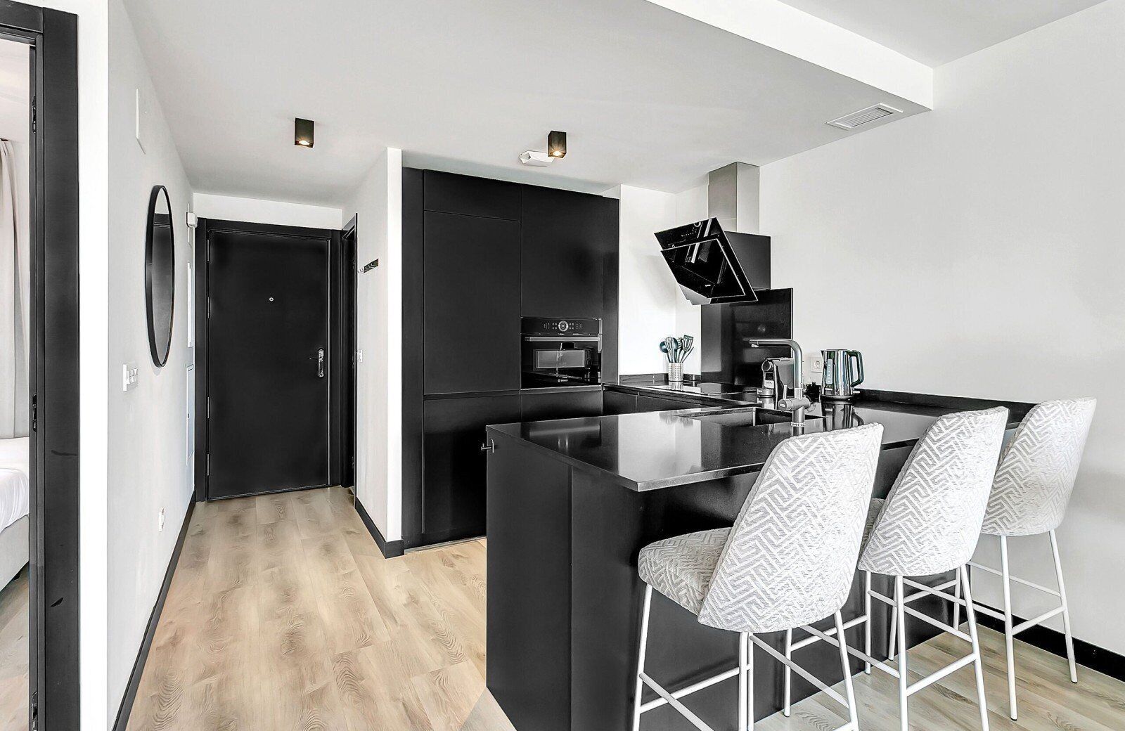 A modern kitchen with a central island, black cabinetry, and a dining area with white chairs.