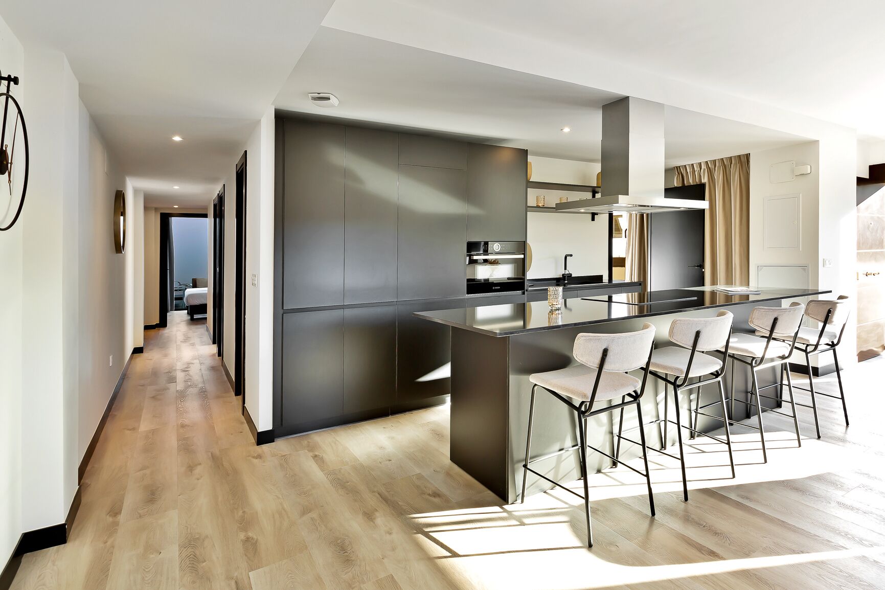 A modern kitchen with a central island, bar stools, and a dining area.