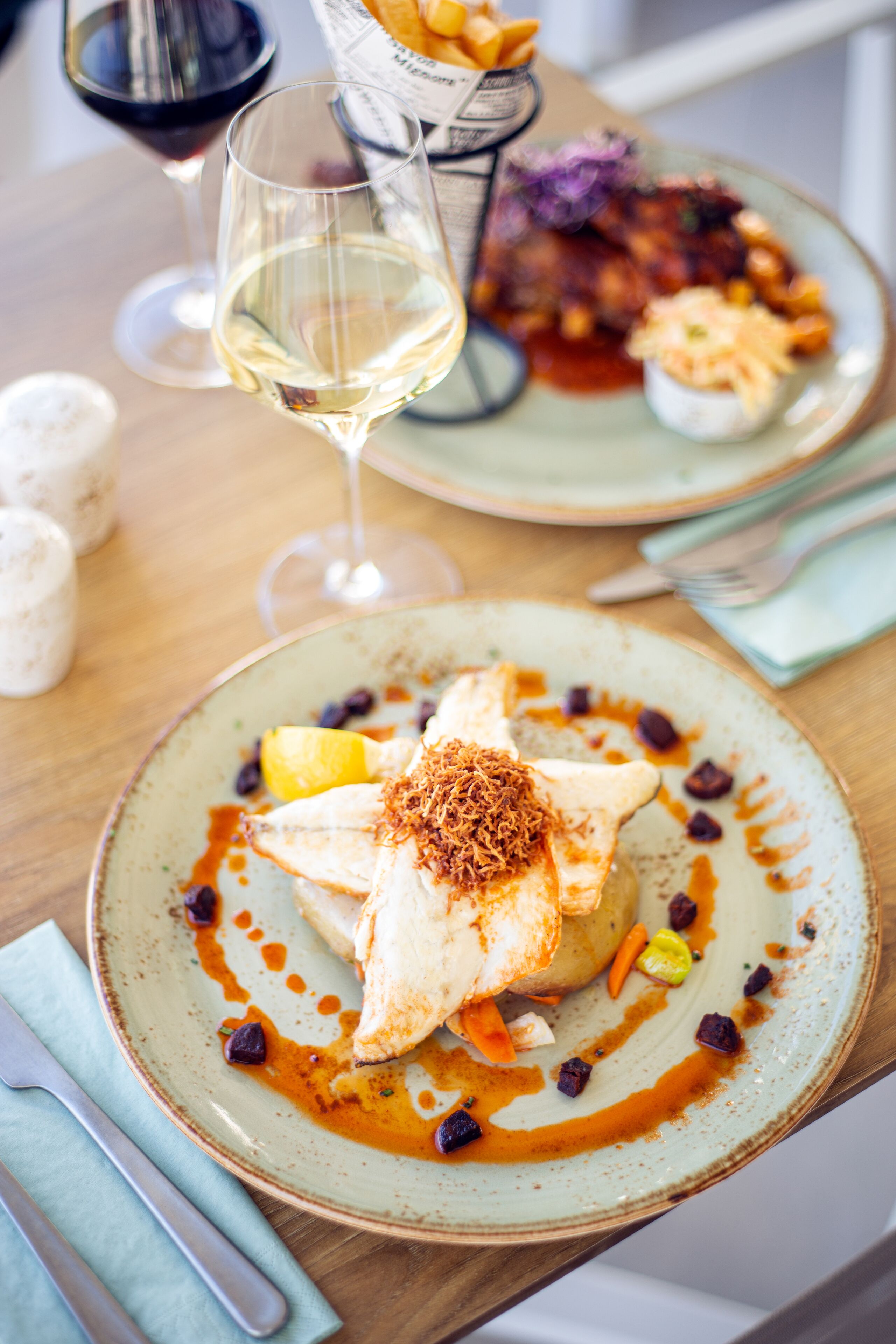 A dining table with plates of food, a wine glass, and a salt shaker.