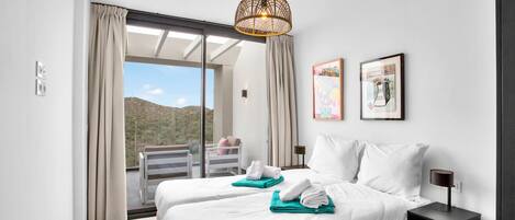 A modern hotel room with a large bed, a bedside table, a hanging light fixture, and a view of the outdoors.
