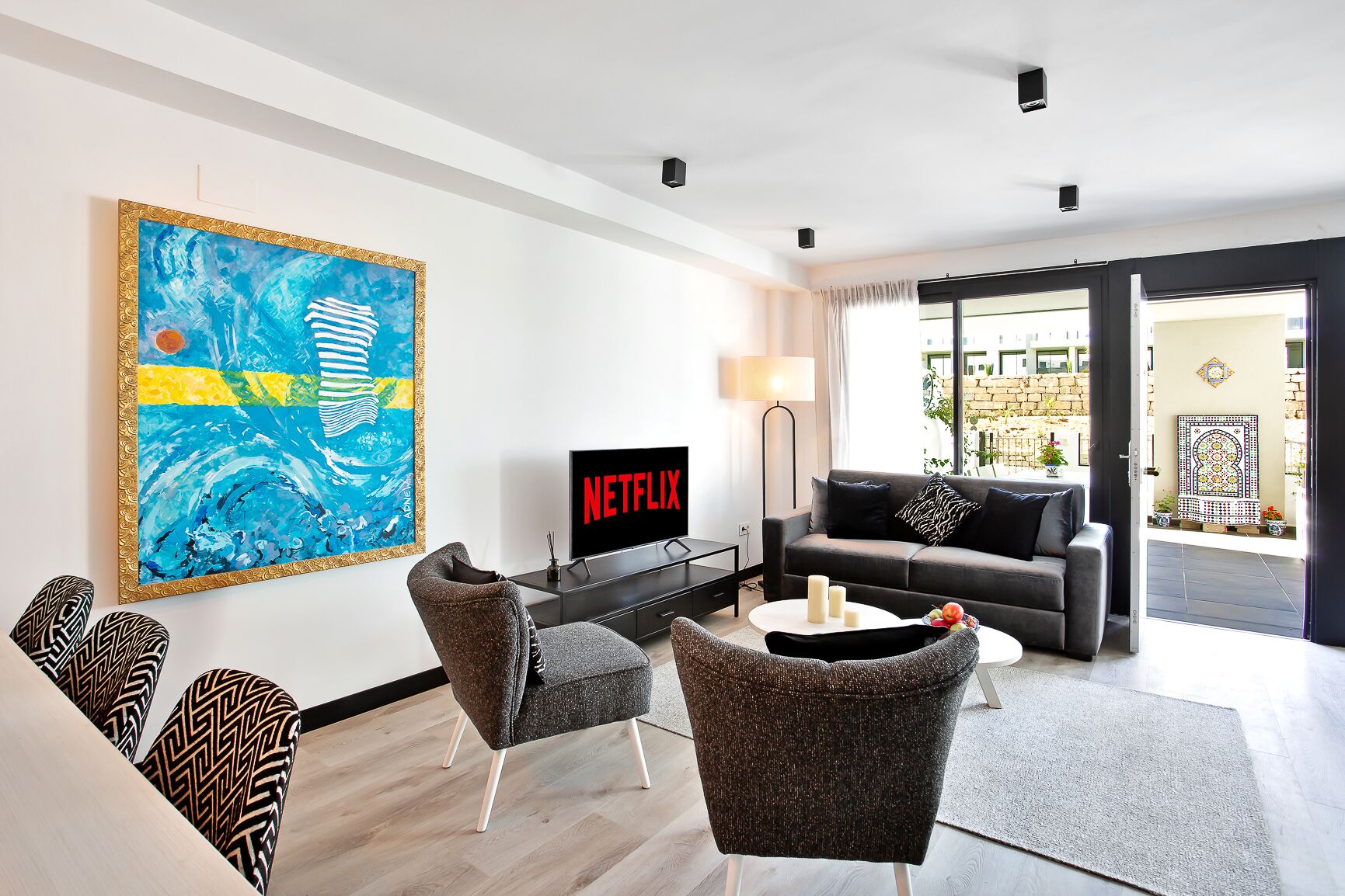 A modern living room with a large abstract painting, a flat-screen TV displaying 'NETFLIX', a grey sofa, and a coffee table.