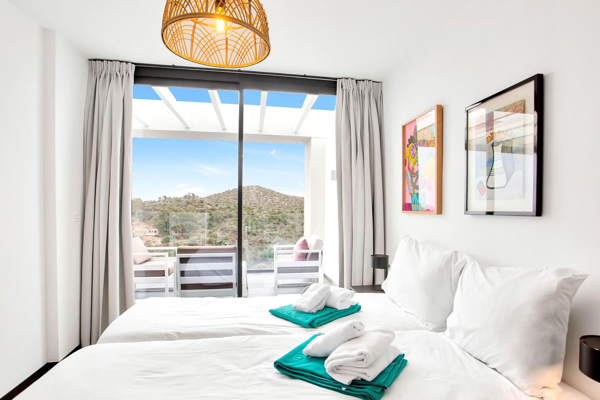 A hotel room with a bed, two towels, a window with curtains, and artwork on the wall.