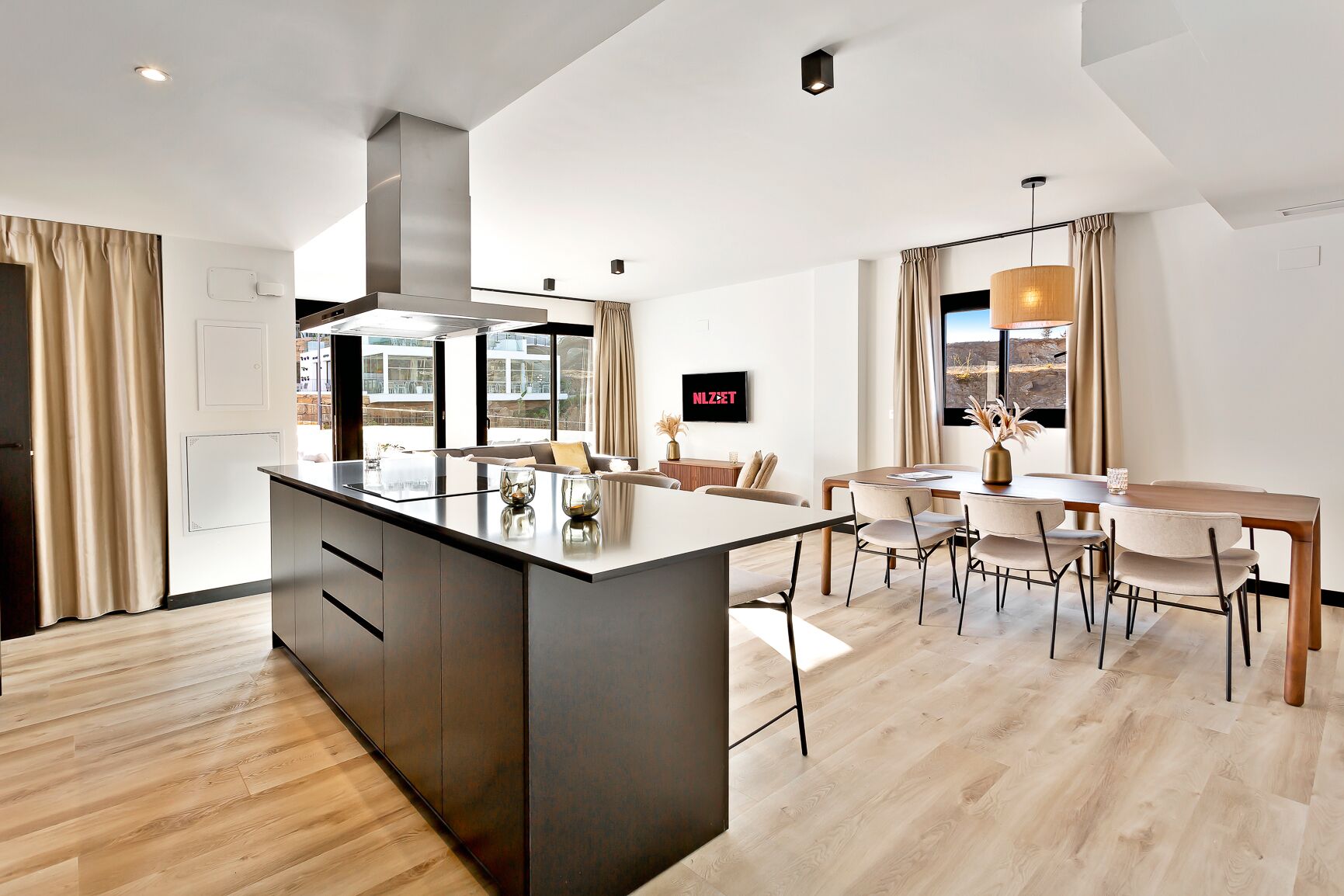 A modern kitchen with a central island, dining area with chairs, and a large window with curtains.