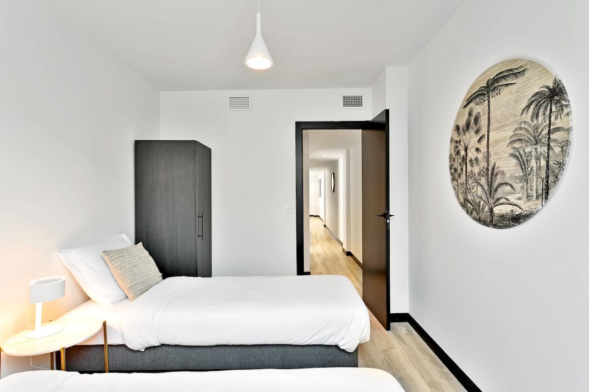 A modern bedroom with a bed, bedside table, wardrobe, and a wall with a tropical artwork.
