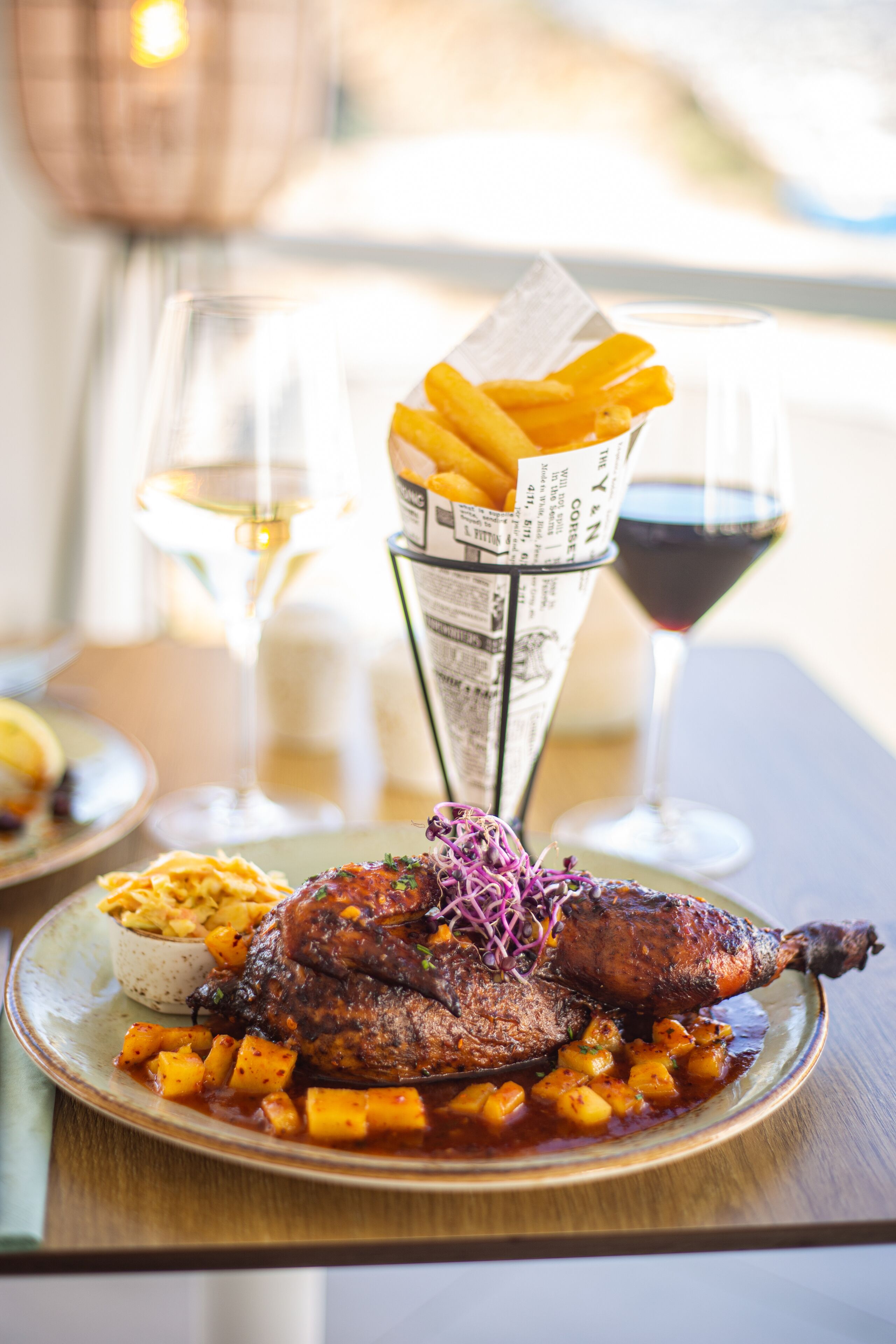 Un plato de comida con pato, papas y papas fritas, acompañado de una copa de vino blanco y una copa de vino tinto.