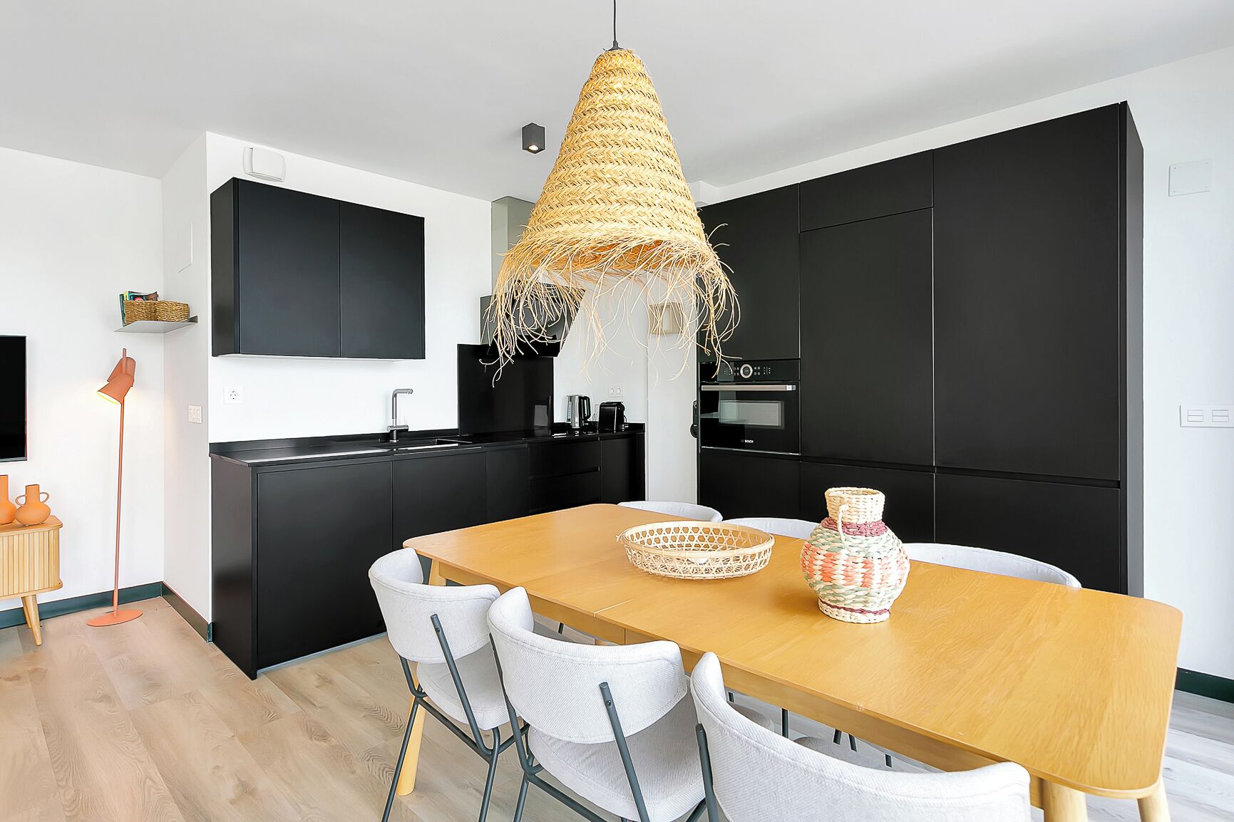 Una cucina moderna con mobili neri, un tavolo da pranzo in legno e sedie bianche.