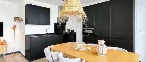 A modern kitchen with black cabinets, a wooden dining table, and white chairs.