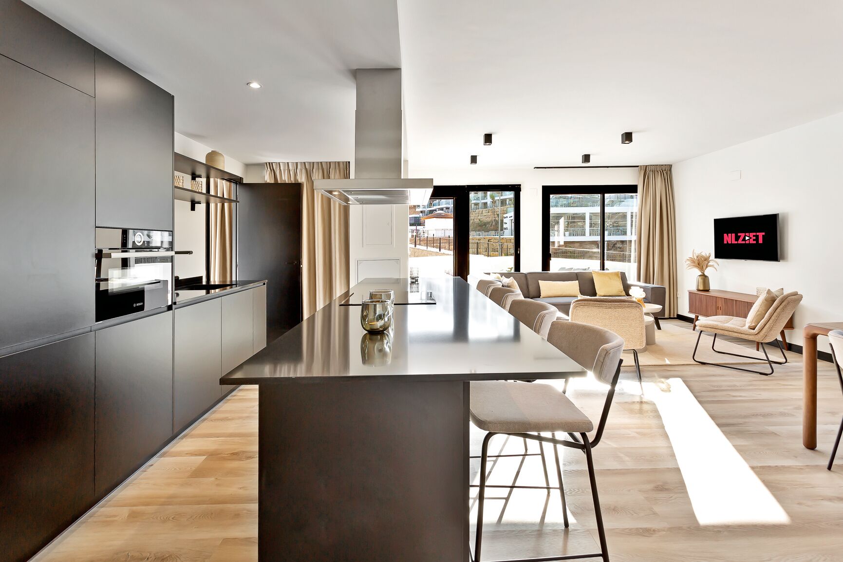 Una cocina moderna con una isla central, un comedor con una mesa larga y una sala de estar con sofá y televisor.