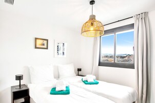 Une chambre d’hôtel avec deux lits, une grande fenêtre donnant sur le paysage, un luminaire suspendu et une petite table avec une lampe.