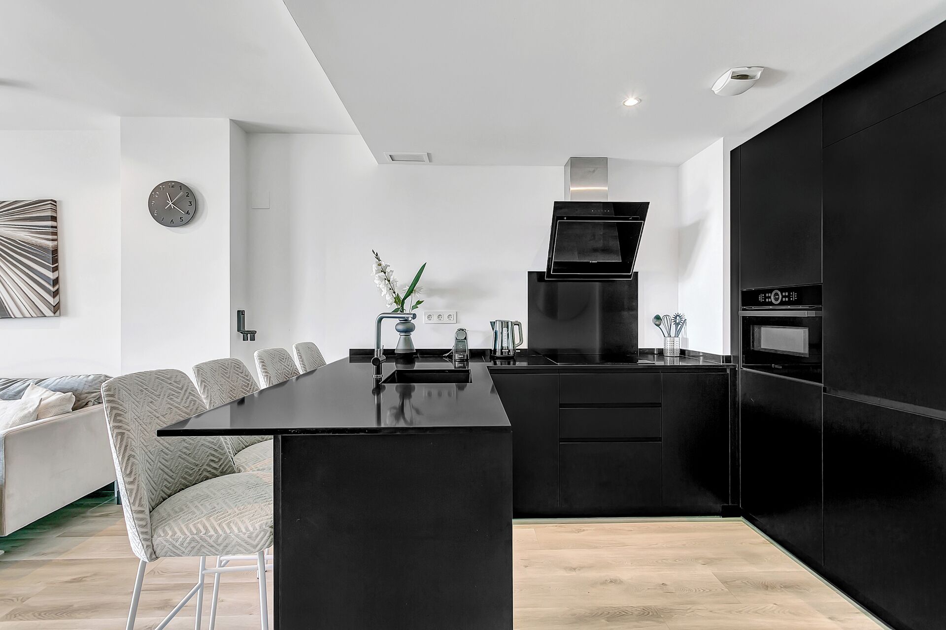 A modern kitchen with a black countertop, stainless steel appliances, and a dining area with a white sofa and patterned chairs.