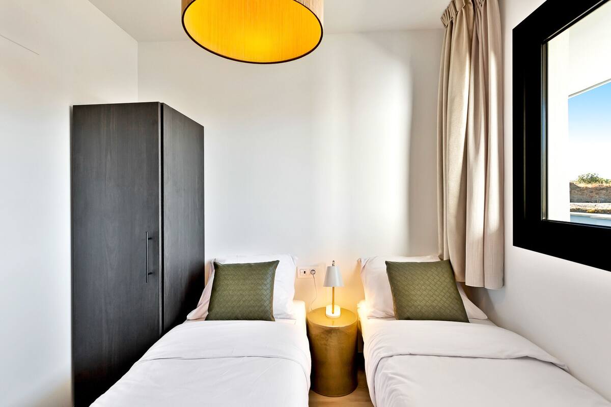 A hotel room with two beds, a wardrobe, a bedside lamp, and a window with curtains.