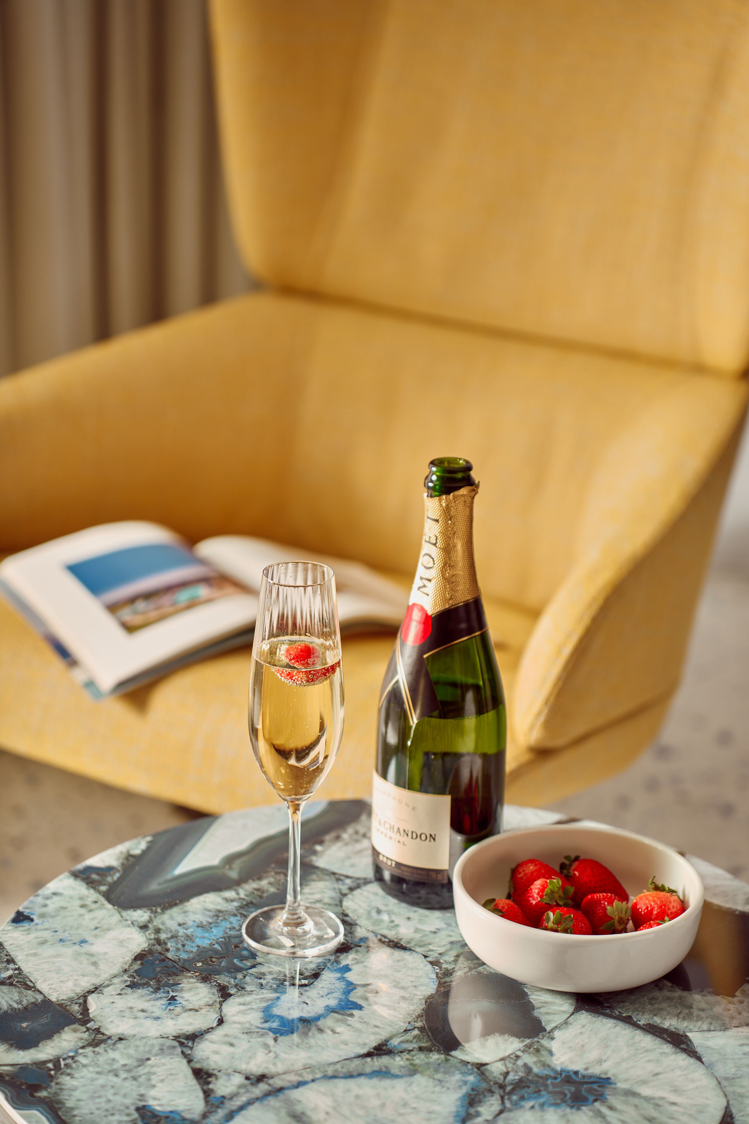 Une bouteille de champagne, un verre de champagne et un bol de fraises sur une table.