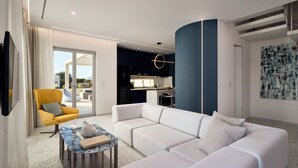Un salon moderne avec un canapé d’angle blanc, un fauteuil jaune et une table basse en marbre. On aperçoit une cuisine à l’arrière-plan.