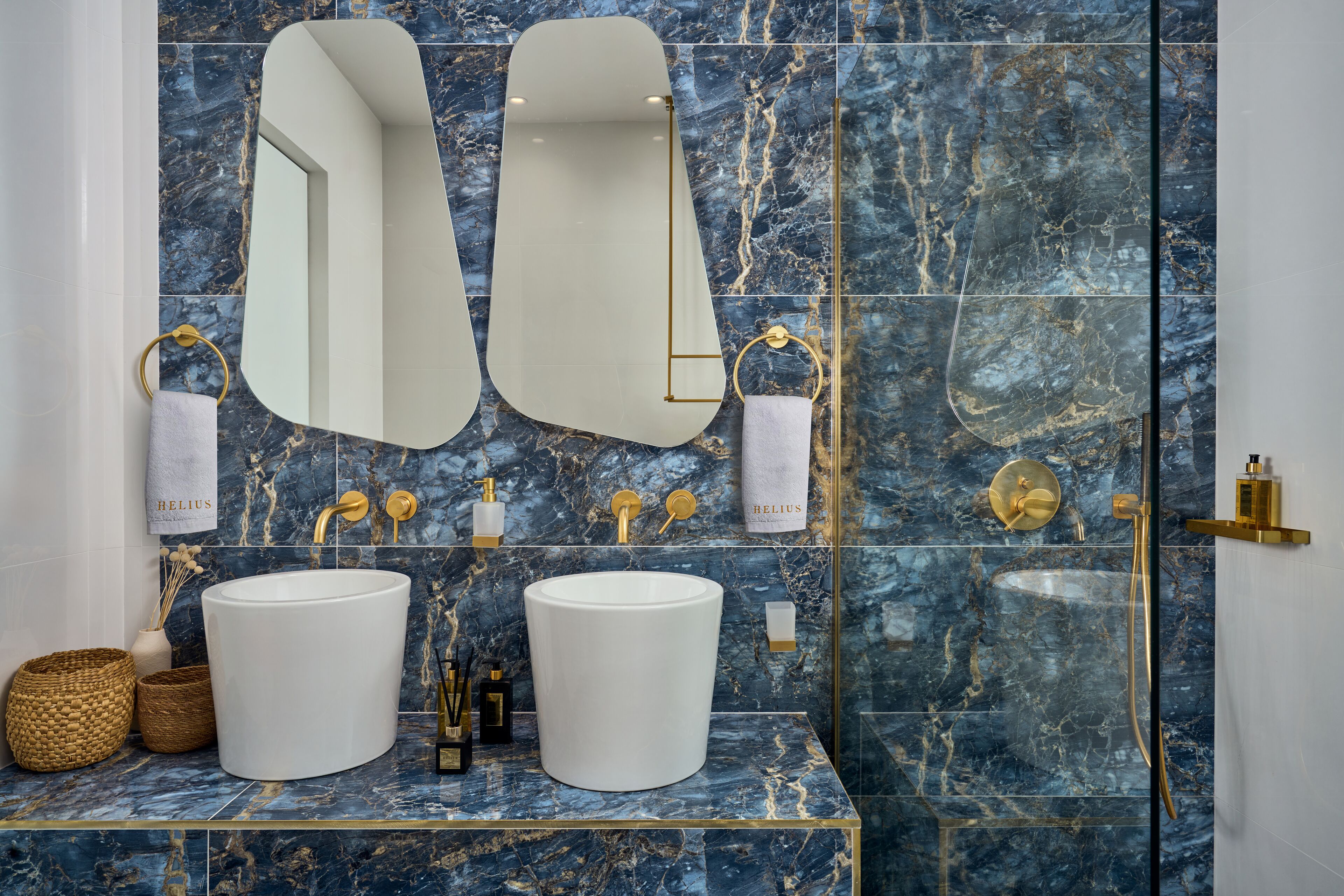 A bathroom with two sinks, marble walls, gold fixtures, and a large mirror.